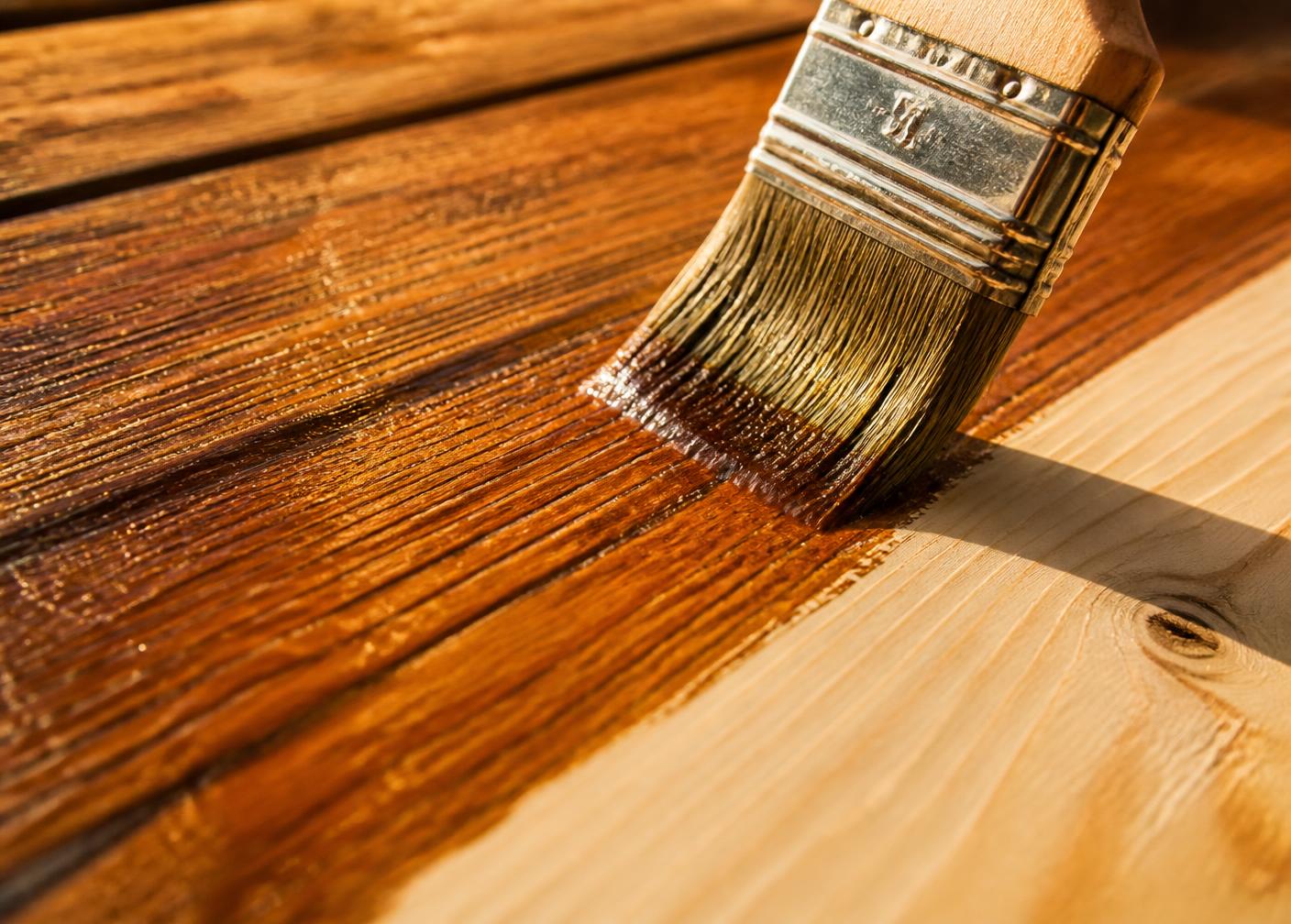 Brush applying rich wood stain, half the boards still bare